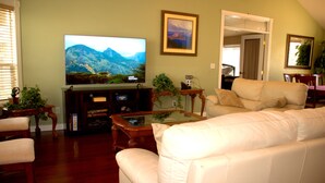 Una sala de estar con un televisor de pantalla plana, una mesa de centro de vidrio y un sofá de cuero blanco.