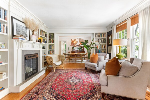 A living room with a fireplace, bookshelves, a dining area, and a sofa.