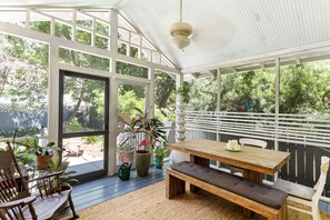 A covered patio with a wooden table and bench, surrounded by potted plants and a view of the backyard.
