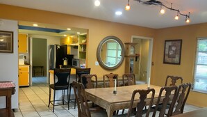 A dining area with a wooden table and chairs, a kitchen in the background, and a round mirror on the wall. - House with HEATED POOL and Outdoor Space (Sarasota)
