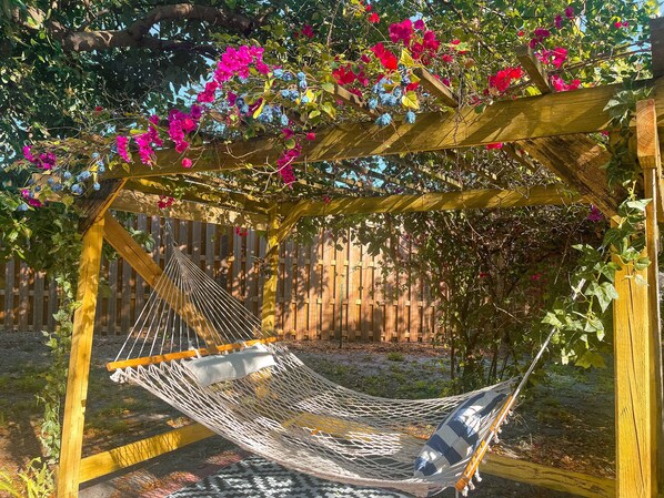 A hammock under a wooden pergola with flowering vines.