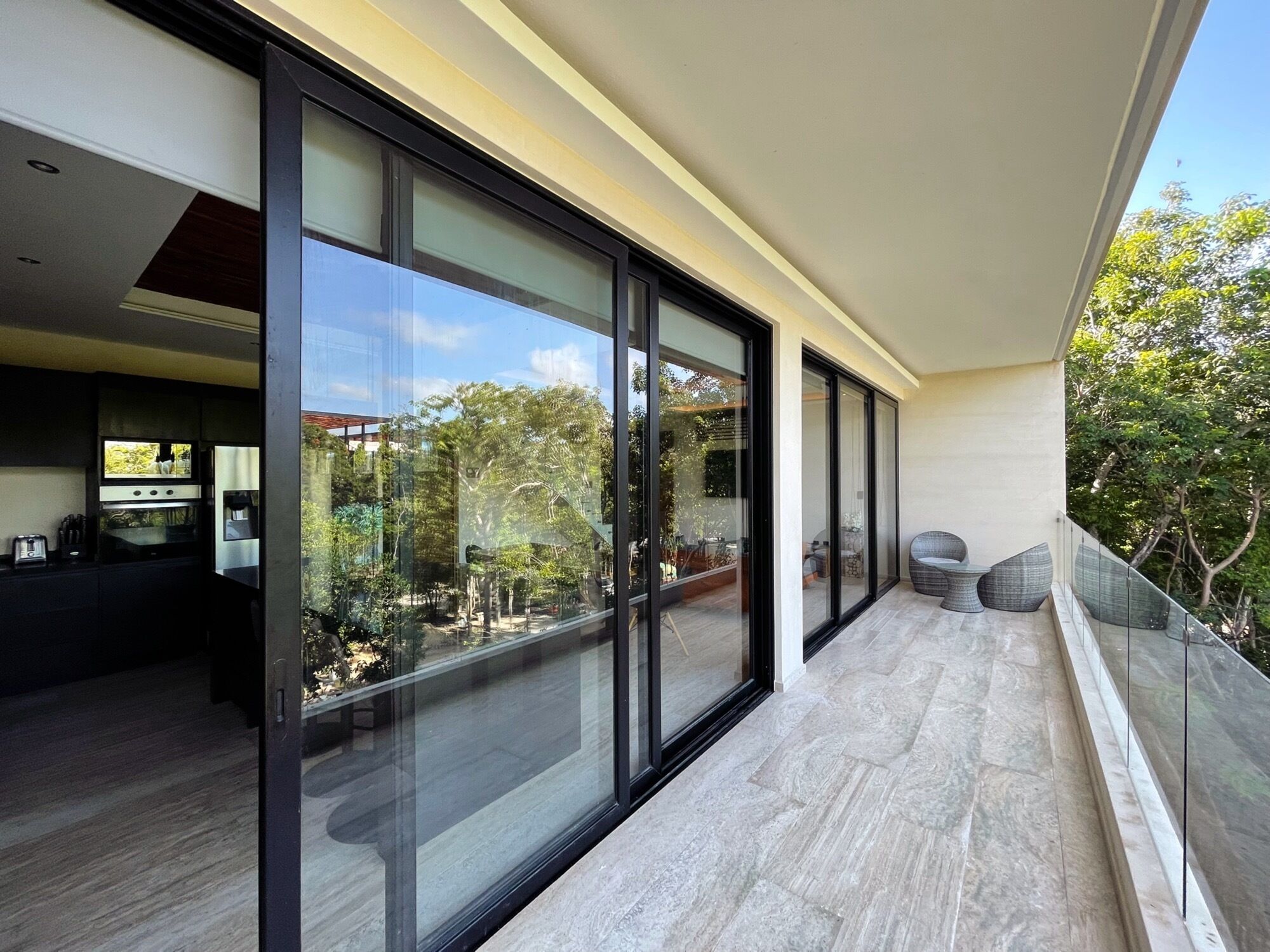 Un balcon moderne avec des portes vitrées, un coin cuisine équipé d’appareils électroménagers et une vue sur les arbres.