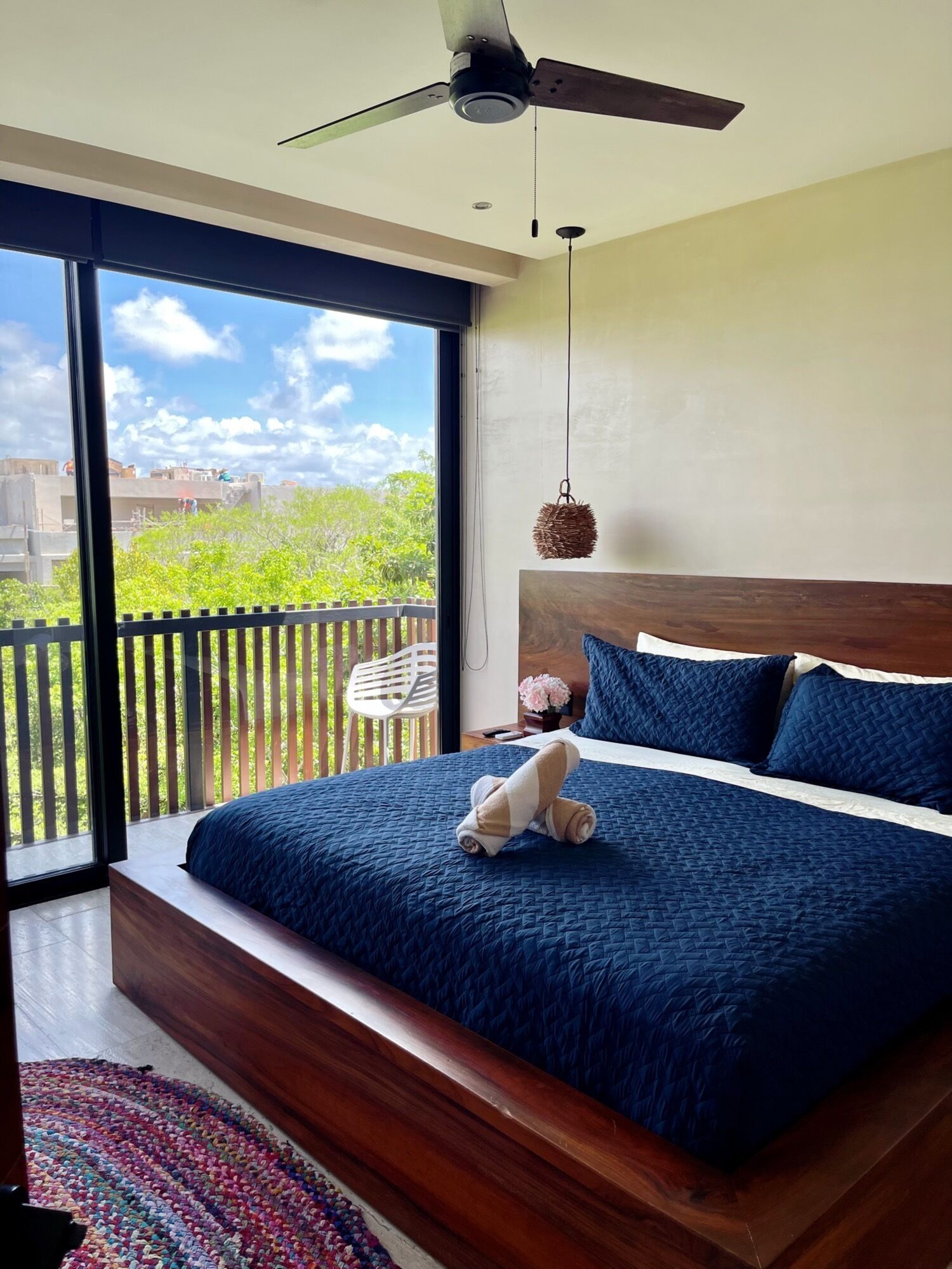 A bedroom with a large bed, a ceiling fan, and a view of a balcony with a railing.