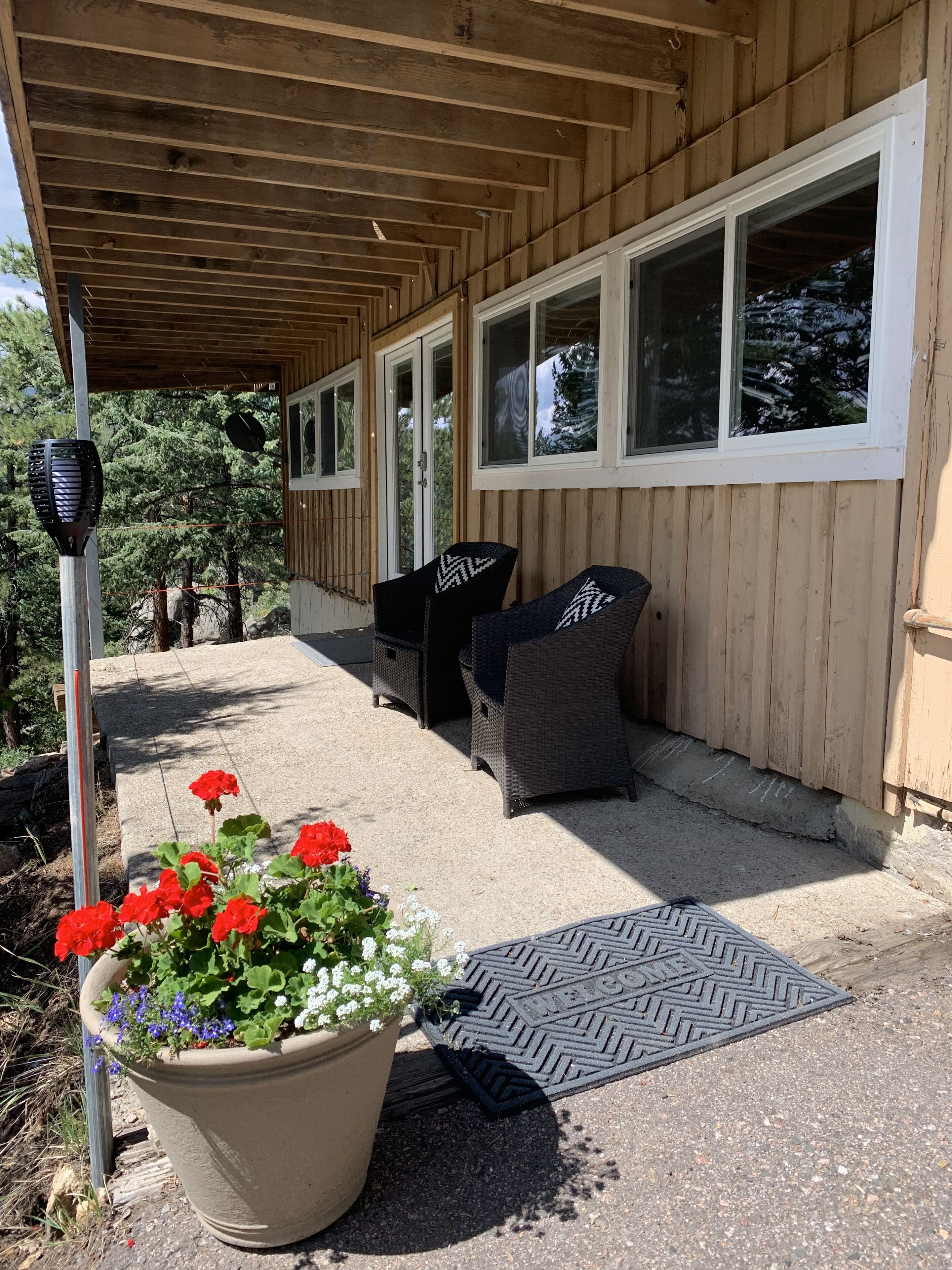 A covered patio area with a seating arrangement, a potted plant with flowers, and a doormat.
