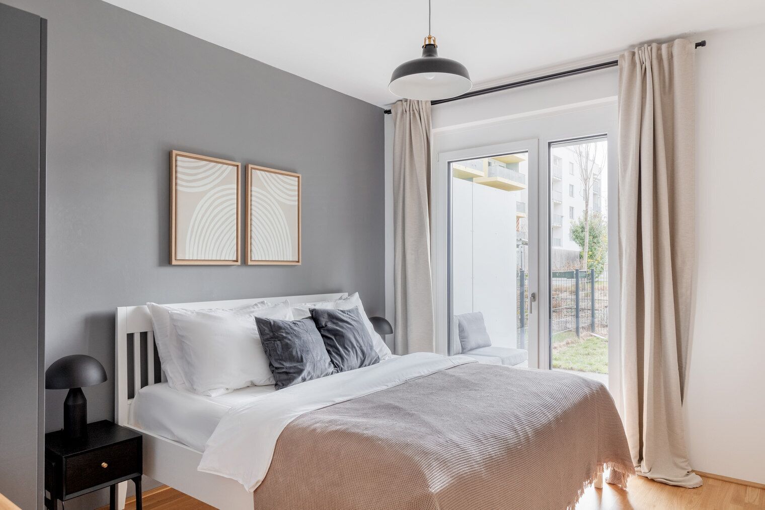 A modern bedroom with a large bed, a bedside table, a lamp, and two framed pictures on the wall.