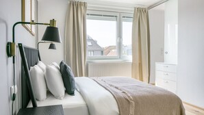 A modern hotel room with a bed, bedside lamp, and a view of the city through a window.