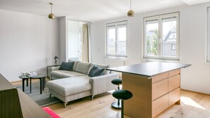 A modern living space with a sofa, a small table, a bar area, and large windows offering city views.