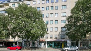 A multi-story building with a row of windows on the ground floor, a visible storefront with signage, and a tree in front.