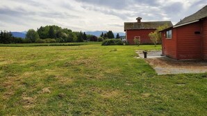 En röd byggnad med en skorsten, en gräsklädd åker och träd i bakgrunden.
