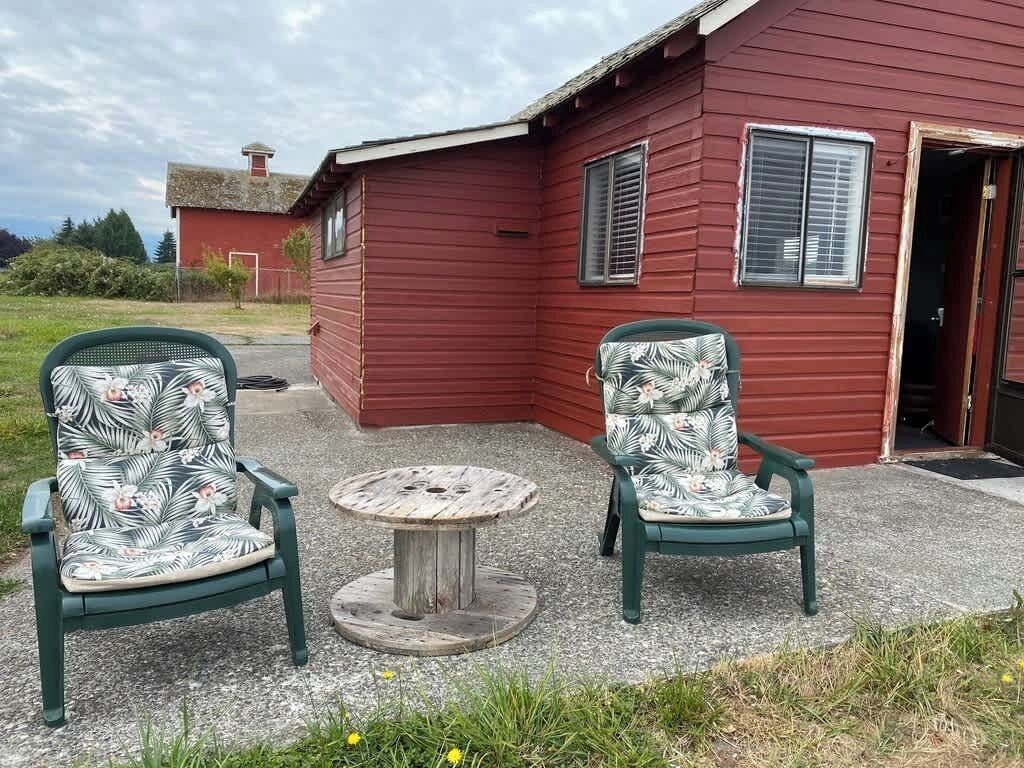 Two green chairs with floral upholstery and a small round table in front of a red building with a door and windows.