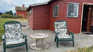 Two green chairs with floral upholstery and a small round table in front of a red building with a door and windows.