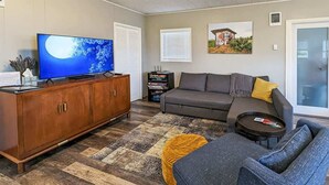 Ett vardagsrum med en platt-TV, en soffa, ett soffbord och en bokhylla.