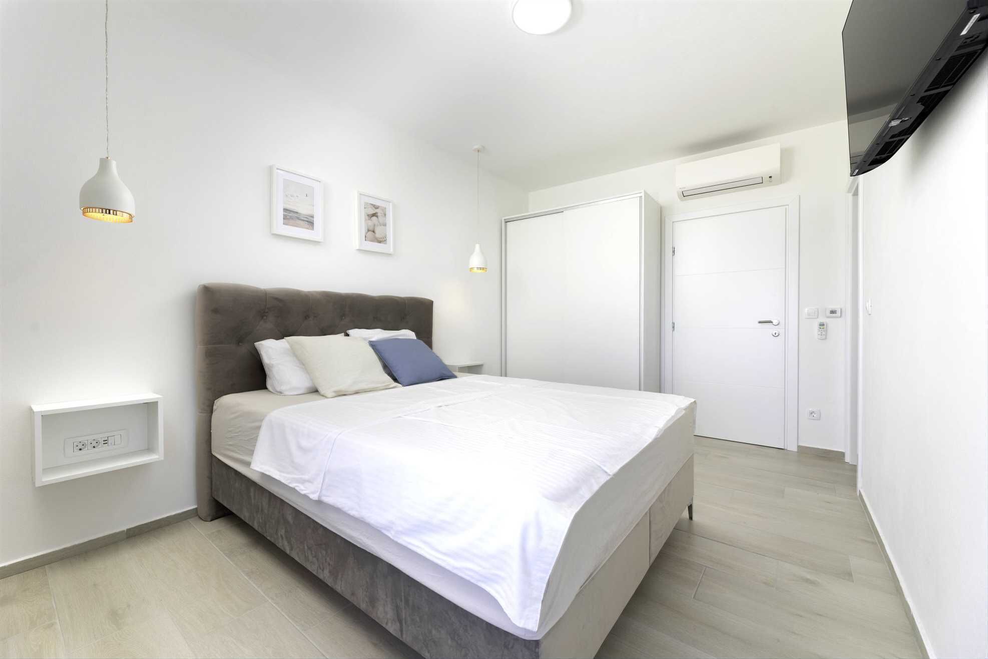 A modern bedroom with a bed, bedside tables, a wardrobe, and a TV mounted on the wall.