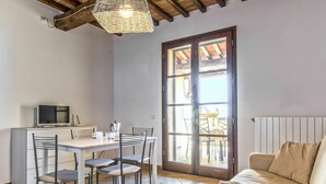 Un coin repas avec une table et des chaises, un téléviseur posé sur un meuble, et une grande fenêtre donnant sur l’extérieur.