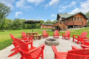 A patio area with red Adirondack chairs, a fire pit, and a wooden cabin in the background. - Mille Lacs Lake Lodge-Game Room-Theatre and More! (Wahkon)