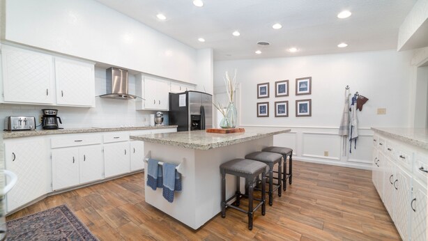 Una cocina moderna con armarios blancos, una isla central con taburetes de bar, un refrigerador de acero inoxidable y una cafetera.