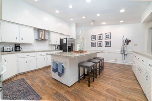 A modern kitchen with white cabinetry, a central island with bar stools, a stainless steel refrigerator, and a coffee maker. - Entire home - Private heated pool, pool table and private yard (Harlingen)