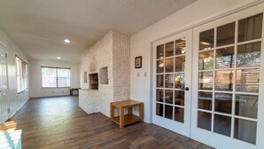 Una habitación amplia con suelo de madera, chimenea de piedra y puerta corrediza de vidrio que da a un espacio exterior.