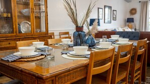 Una mesa de comedor dispuesta con cuencos y platos blancos, rodeada de sillas de madera.