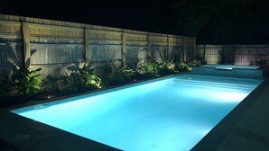 Una piscina rectangular con valla de madera y plantas a su alrededor.