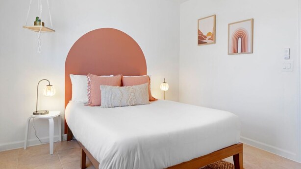 Une chambre à coucher comprenant un lit, deux tables de chevet, un luminaire suspendu et deux cadres photos fixés au mur.
