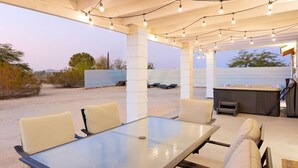 Une terrasse extérieure avec une table et des chaises en verre, des guirlandes lumineuses et un jacuzzi.