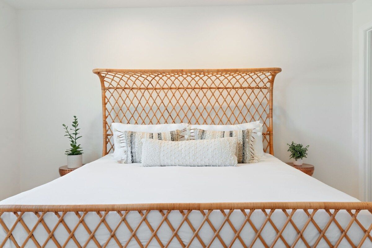 A bed with a woven headboard, white bedding, and two small potted plants on either side.