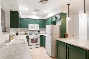 A modern kitchen with green cabinets, white appliances, and a marble countertop.