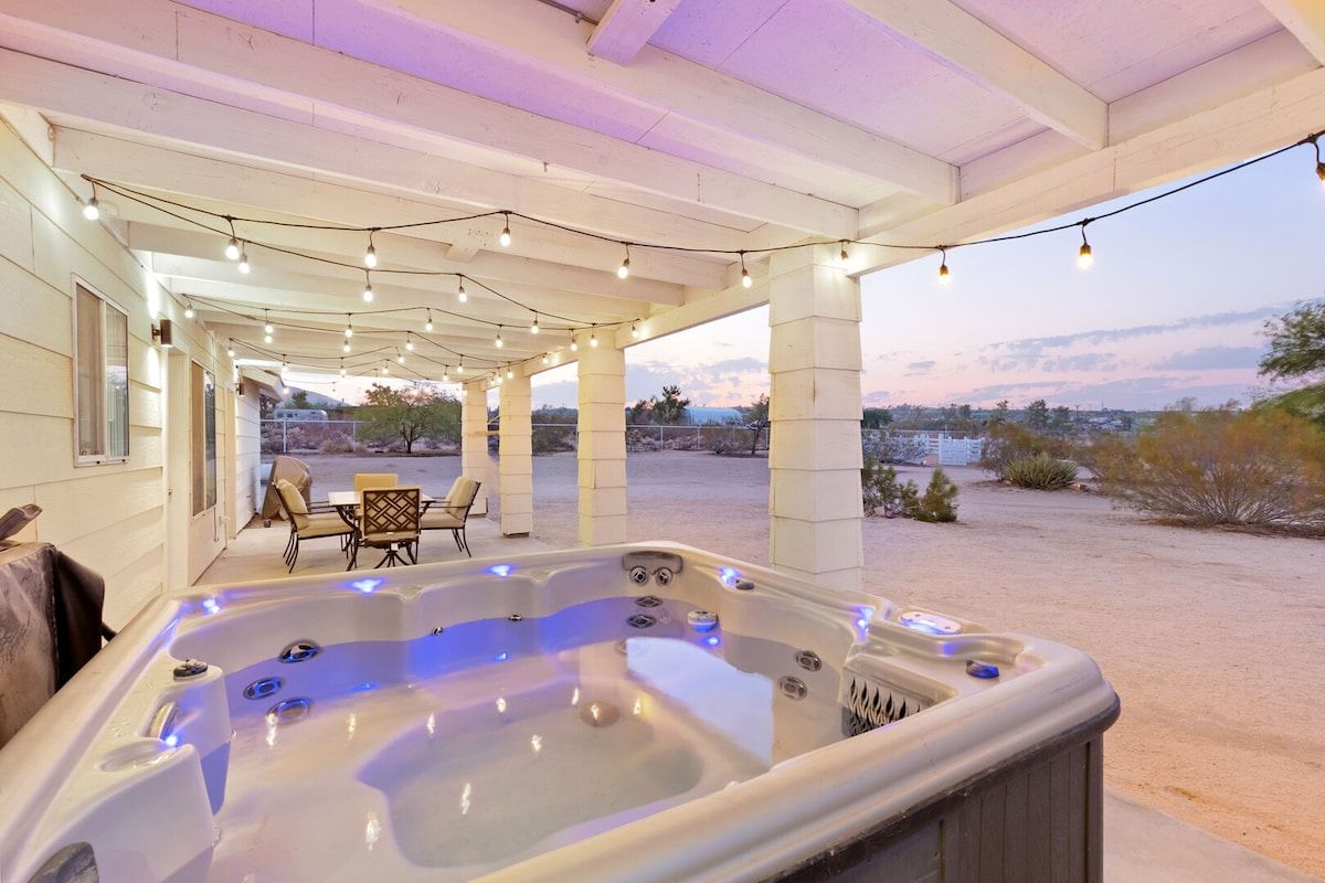 A covered outdoor area with a hot tub, string lights, and a table with chairs.