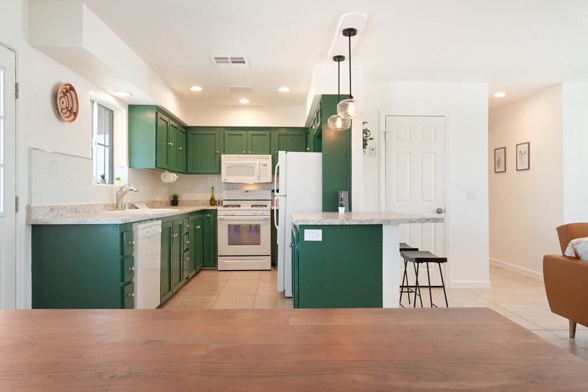 Une cuisine moderne avec des meubles verts, des appareils électroménagers blancs et un plancher en bois.