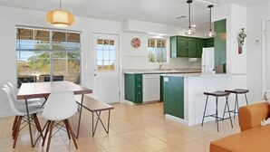 Une cuisine moderne avec un coin repas, dotée d’une grande fenêtre, de meubles de couleur verte et d’un bar.