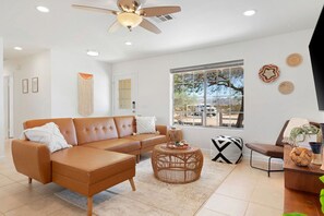 A modern living room with a brown leather sofa, a round wicker coffee table, and a ceiling fan.