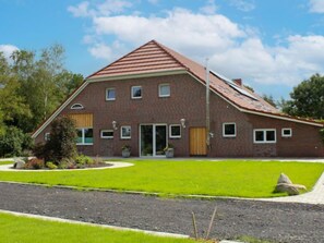 Une maison à deux étages, construite en briques et coiffée d’un toit rouge, avec une porte d’entrée et un petit jardin devant, comprenant une pelouse et un chemin.