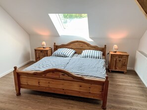 Un lit en bois dans une pièce dotée d’un plafond en pente et d’un puits de lumière, deux tables de chevet avec des lampes et un radiateur.