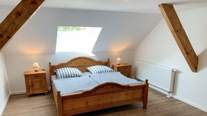 Une chambre à coucher avec un lit en bois, deux tables de chevet, une fenêtre et un radiateur.