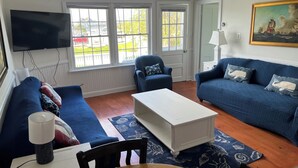 A living room with a blue sofa, a white coffee table, and a blue armchair. There is a television mounted on the wall and a painting above the sofa.