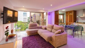 A modern living room with a sofa, a dining table with chairs, a kitchen area, and a balcony with a view of buildings. - Apartment with Jacuzzi near the beach, Arenales (Los Arenales del Sol)