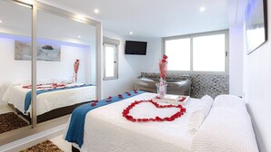 A hotel room with a large mirror, a bed with rose petals, a massage table, a bathtub, and a TV on the wall. - Apartment with Jacuzzi near the beach, Arenales (Los Arenales del Sol)