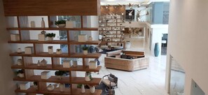 A spacious lobby with a wooden shelving unit displaying various decorative items, a seating area with a sofa and chairs, and a staircase leading to an upper level.