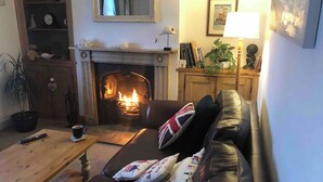 Ein gemütliches Wohnzimmer mit Kamin, einer Ledersofa mit Kissen, einem Holztisch und einem Bücherregal.