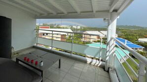 Un balcon avec un sol carrelé, une table décorée de bougies rouges et une vue sur des immeubles et un arc-en-ciel.