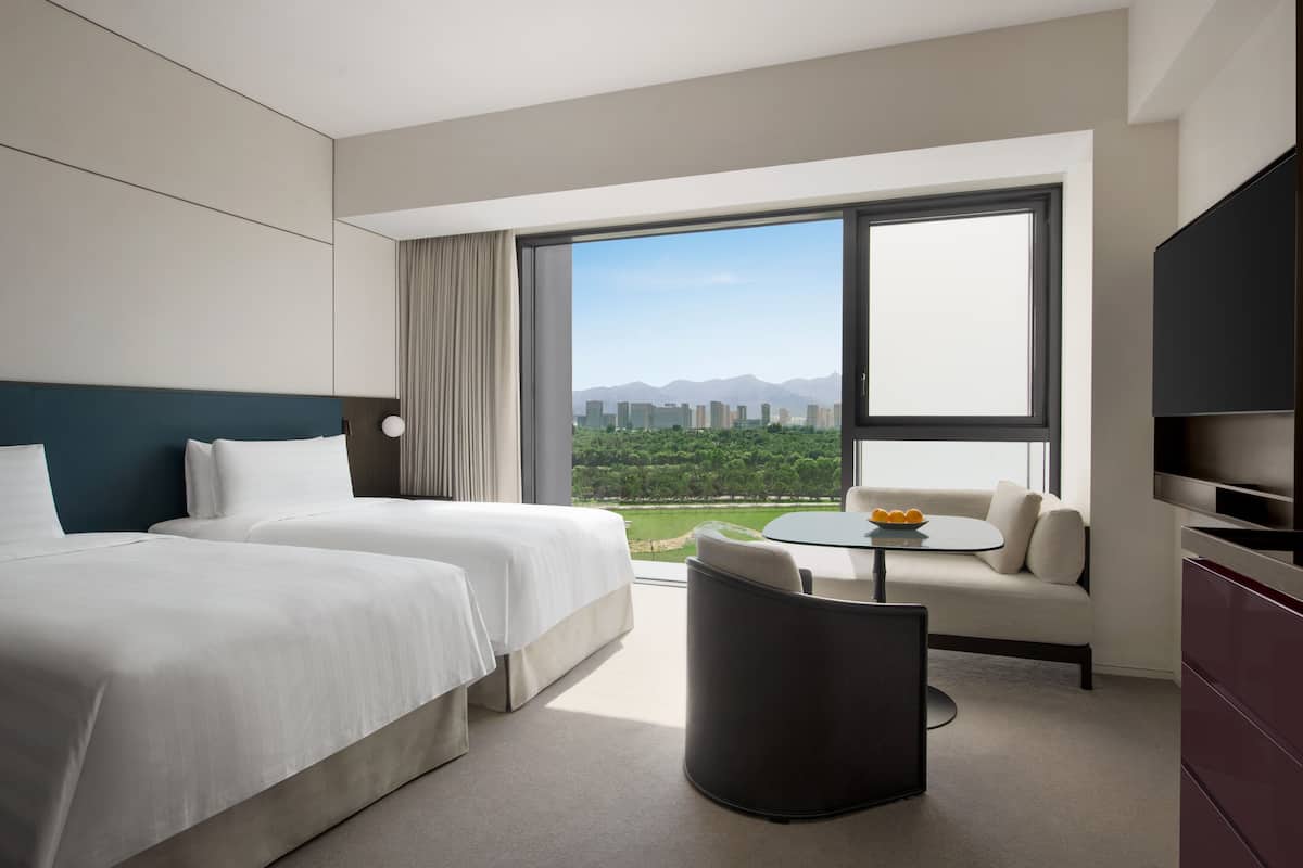 Een hotelkamer met twee bedden, een bank, een eettafeltje en een televisie.