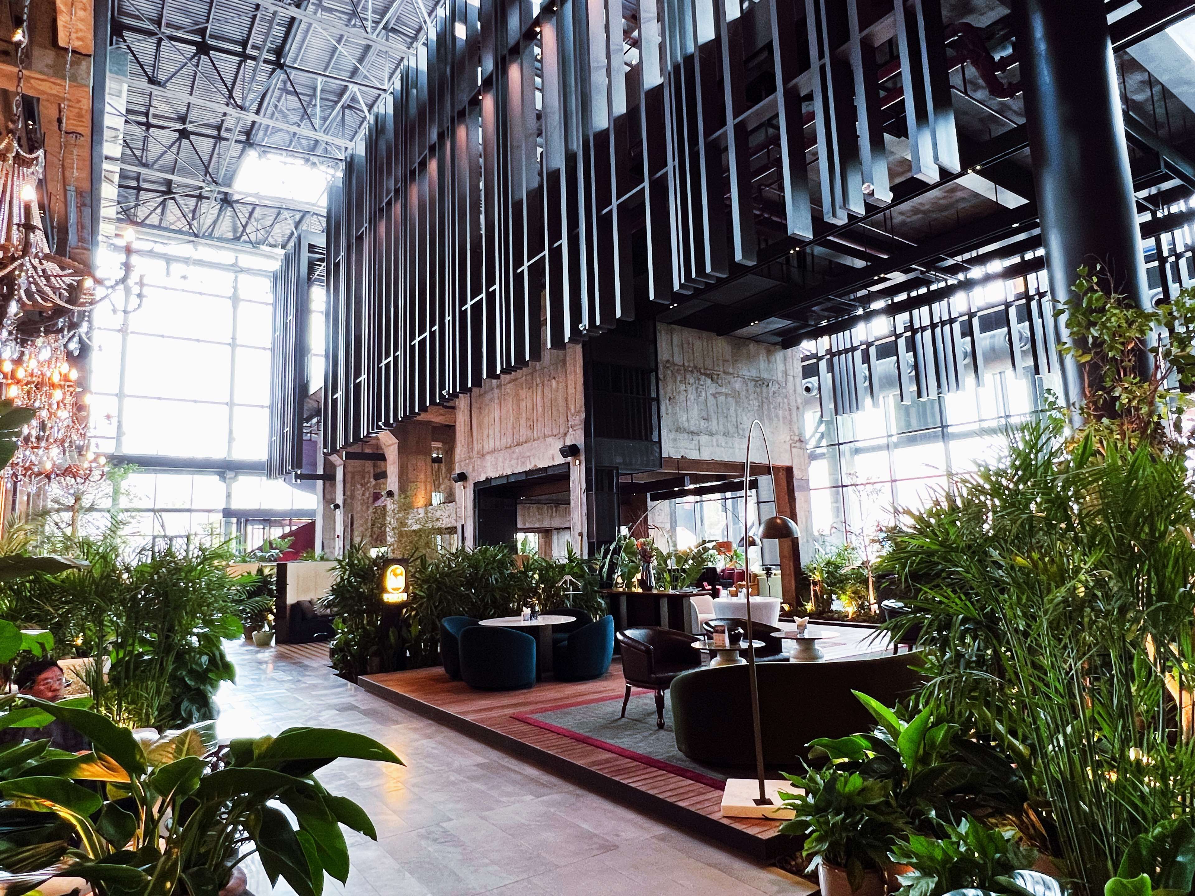 A spacious indoor area with high ceilings, modern furniture, and abundant indoor plants.