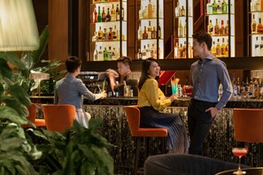 Una zona de bar con mostrador de mármol, sillas color naranja y una variedad de botellas en estanterías.