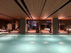 Un área de piscina interior moderna con sillones reclinables y una escalera que lleva a un nivel superior.