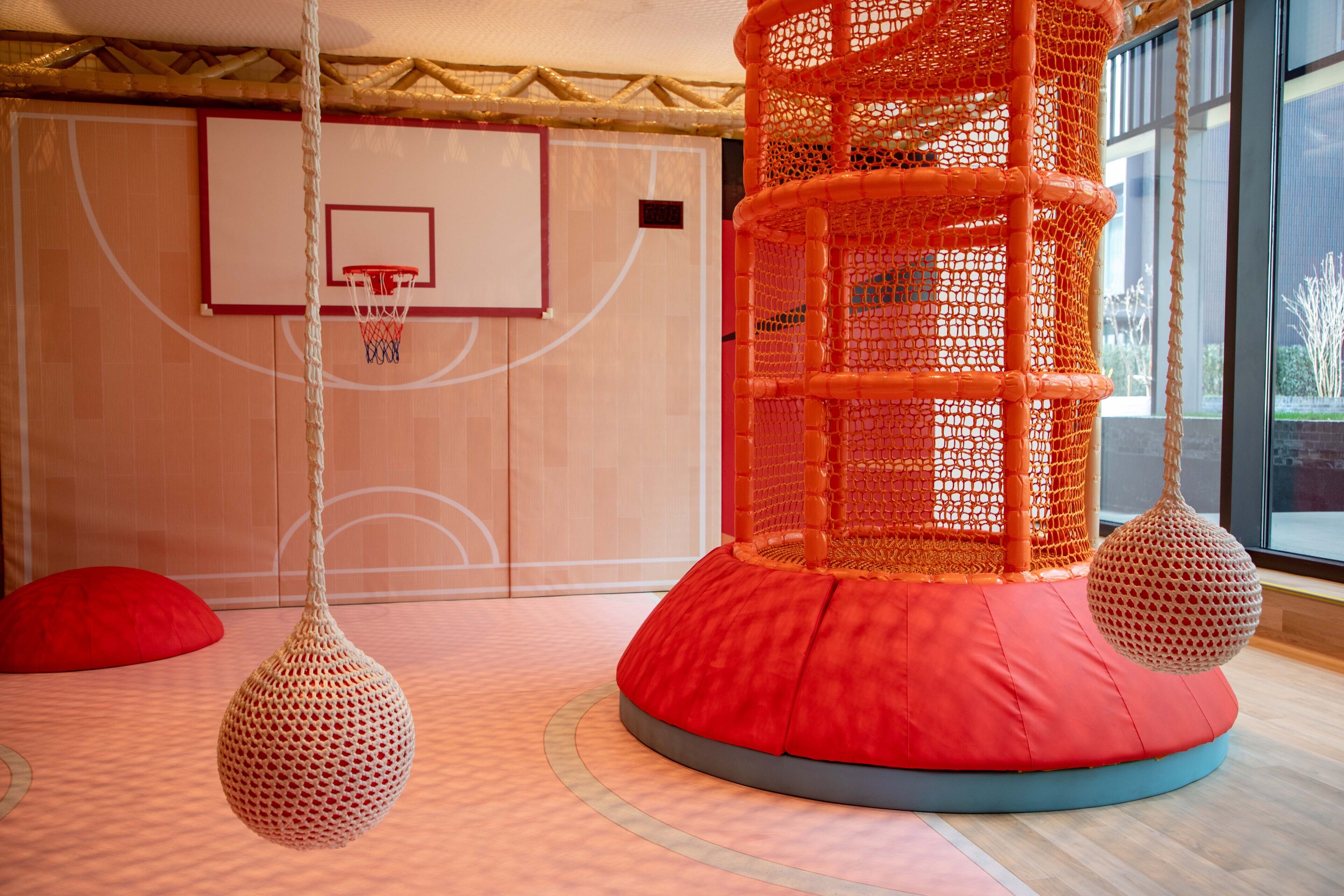 A basketball court with a net, a red cushioned play area, and hanging spherical decorations.