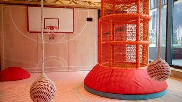 A basketball court with a net, a red cushioned play area, and hanging spherical decorations.
