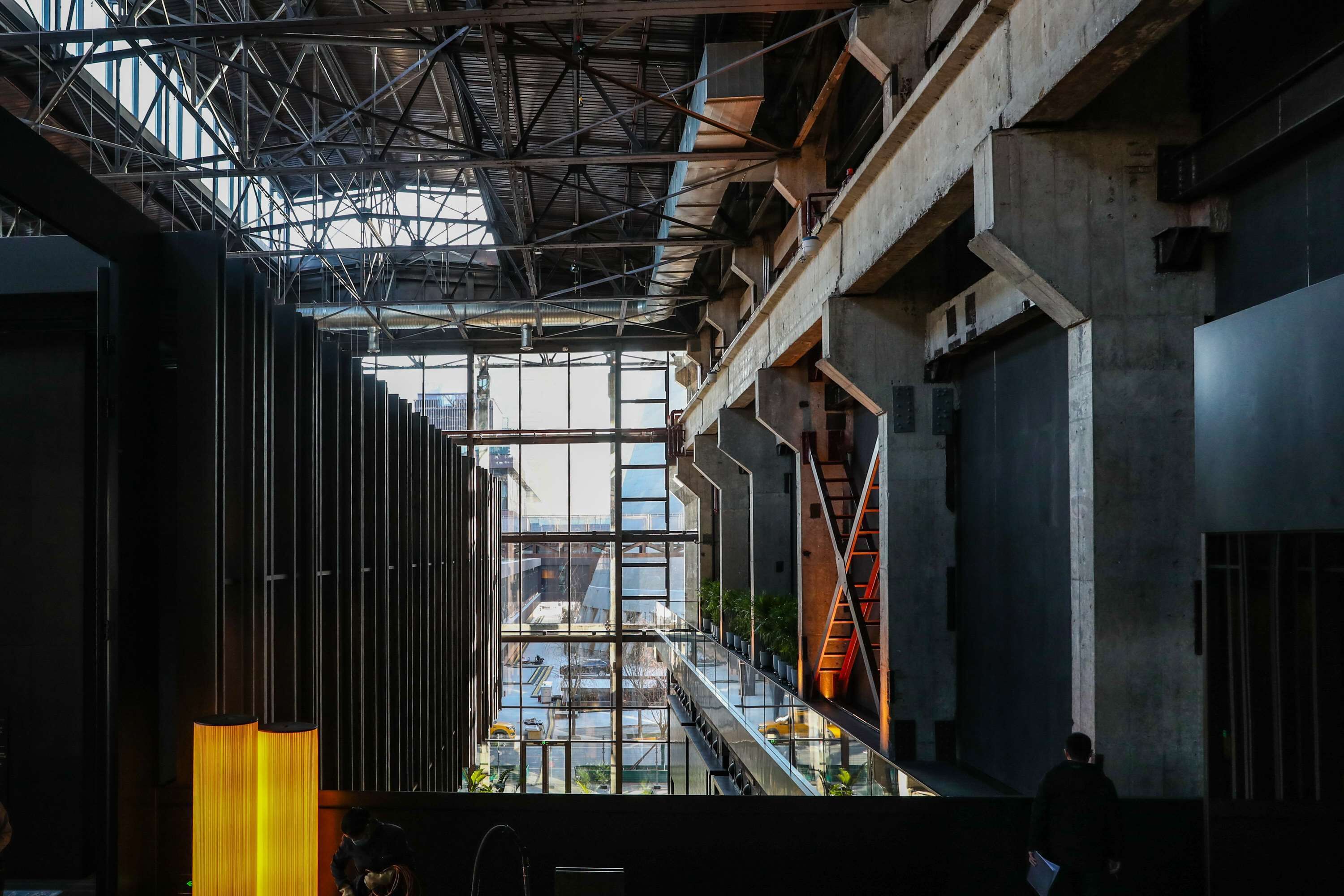 An interior view of a modern building with a high ceiling, visible structural beams, and a glass facade.