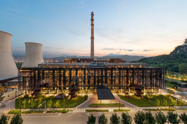 Un edificio moderno con amplios ventanales de vidrio, una torre destacada y torres de refrigeración.