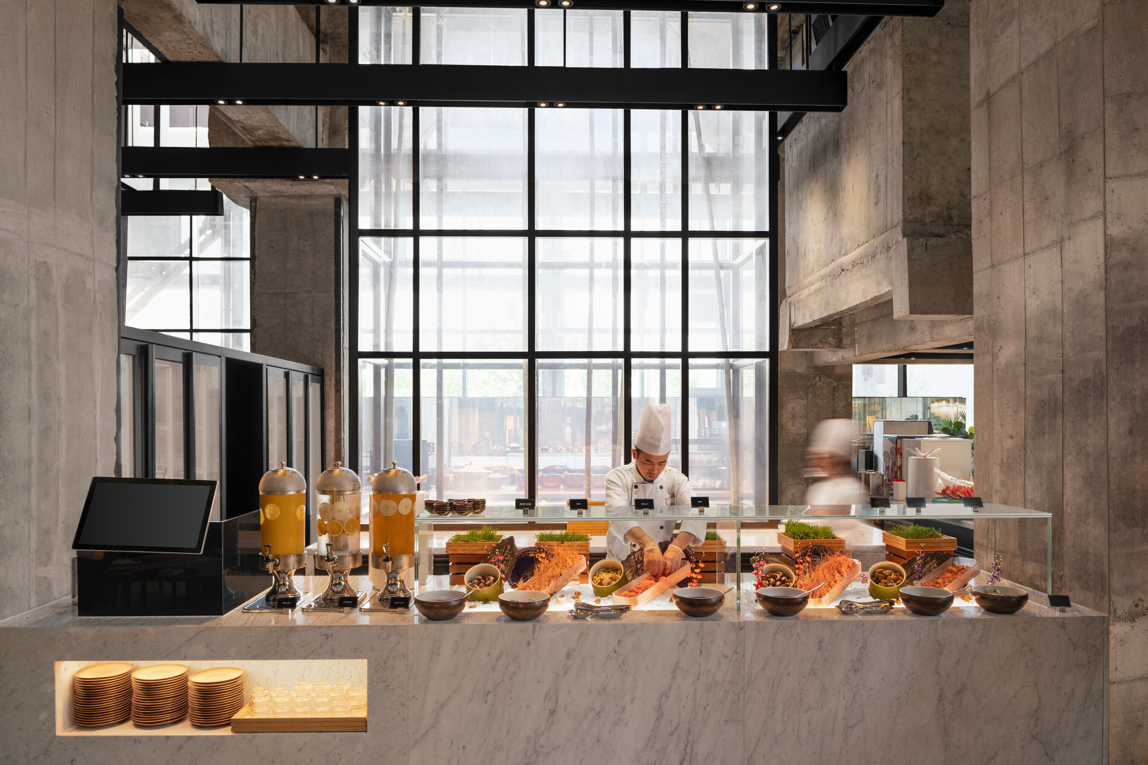 Una cocina moderna con un chef preparando comida, ventanas amplias y una encimera de mármol.